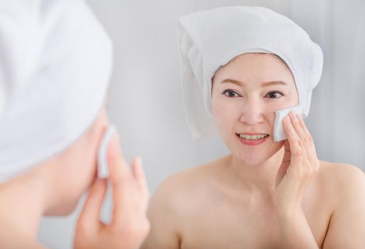 Beautiful woman looking mirror and cleaning her face with cotton