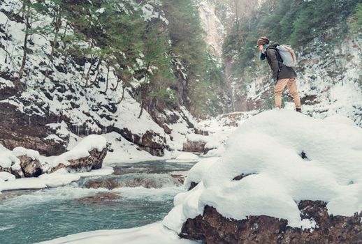 Hiker young woman with backpack looking at mountain river in winter