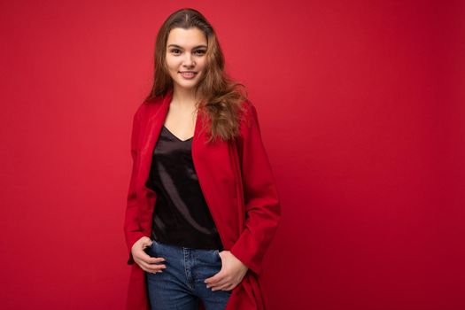 Young beautiful european stylish brunette woman wearing black blouse top and red cardigan isolated over red background with positive sincere emotions. Simple and natural looking at the camera. Free space.