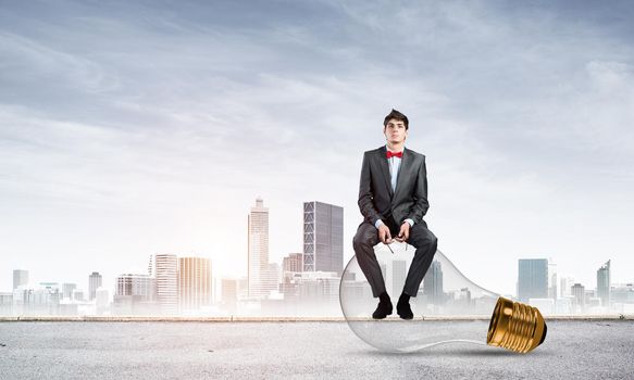 A businessman with glasses sits on a light bulb. concept of creativity in business