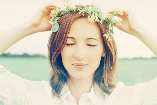 Beautiful woman with closed eyes with wreath of yellow wildflowers on her head in summer