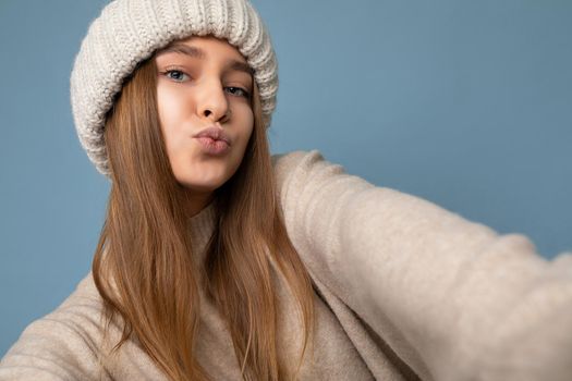 Closeup shot of beautiful sexy positive young dark blonde woman isolated over colourful background wearing everyday trendy clothes looking at camera and giving kiss, concept of selfie photo.
