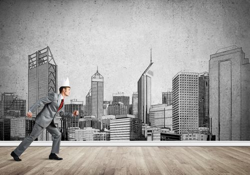 Young handsome businessman wearing white paper crown running in a hurry
