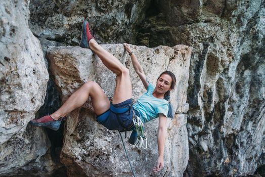 Beautiful sporty girl in safety harness with equipment started to climb the rock wall outdoor, looking at camera