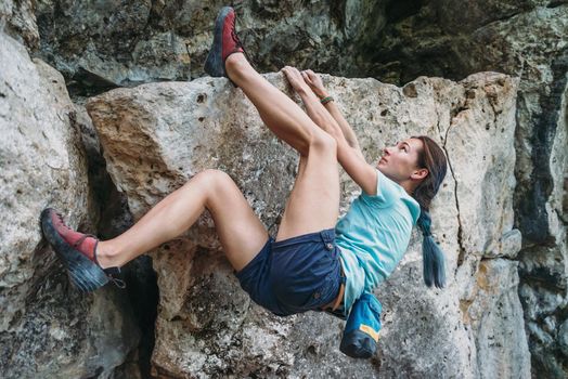 Beautiful sporty young woman started to climb the rock outdoor, bouldering