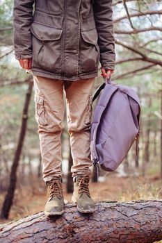 Unrecognizable traveler woman standing on tree trunk with backpack in the forest outdoor. Hiking and leisure theme