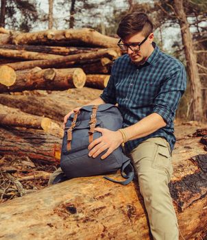 Hiker young man with backpack sitting on felled wood trunk outdoor