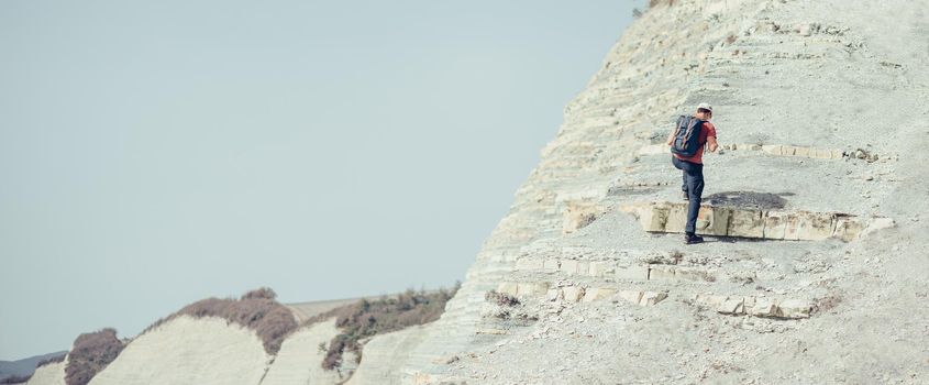 Hiker young man with backpack climbing on stone mountain outdoor