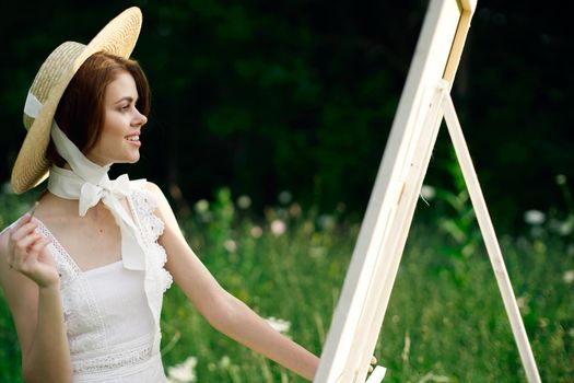 Woman in white dress paints a picture on nature easel. High quality photo