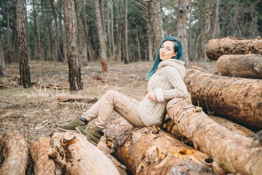 Beautiful young woman sitting on stack of tree trunks in the forest, looking at camera. Young woman resting on nature outdoor