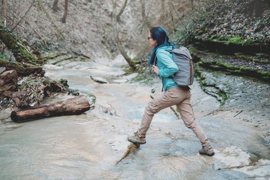 Hiker young woman with backpack crossing the mountain river outdoor