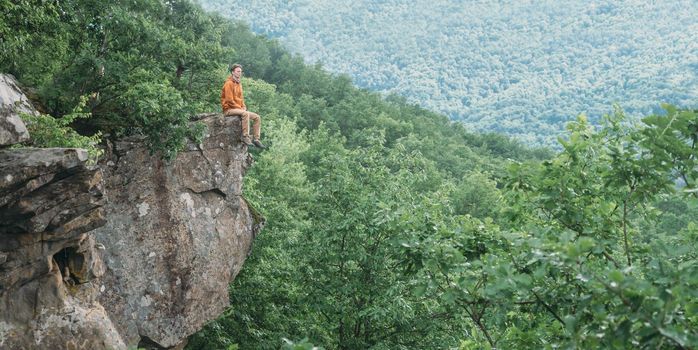 Traveler young man sitting on edge of cliff and enjoying view of nature in summer outdoor