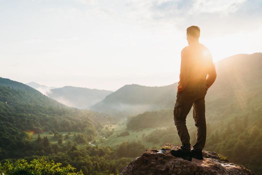 Traveler young man standing in the summer mountains at sunset and enjoying view of nature