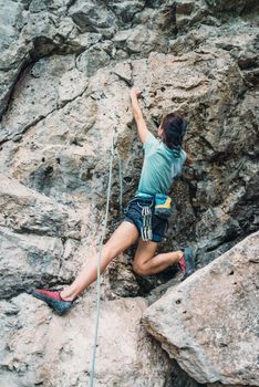 Sporty young woman in safety harness with equipment climbing the rock wall outdoor