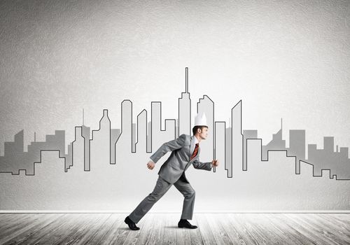 Young handsome businessman wearing white paper crown running in a hurry