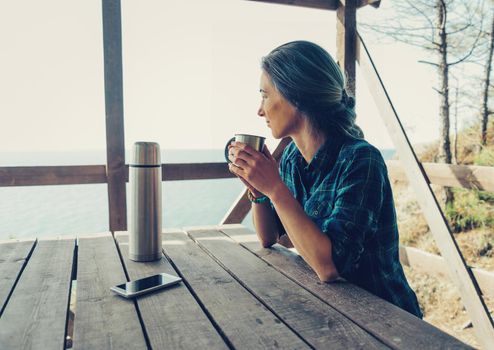 Young woman resting with cup of tea on wooden terrace in summer