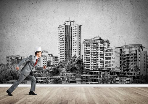 Young handsome businessman wearing white paper crown running in a hurry