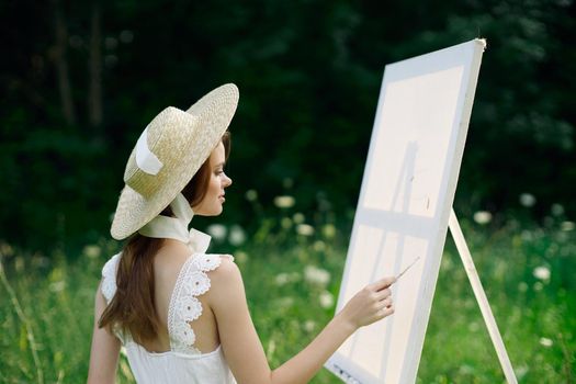 Woman in white dress in nature paints a picture of a landscape hobby. High quality photo