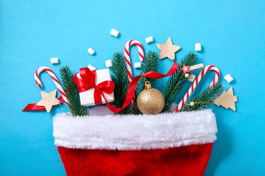 Creative Christmas Concept with Santa Hat, Fir Tree, Gift Box, Ball and Candys on Blue Background. Top View. Flat Lay.