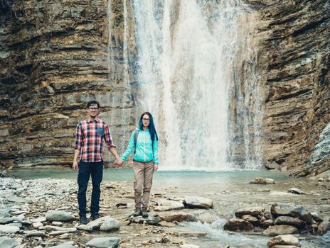 Explorer young couple standing on background of waterfall outdoor