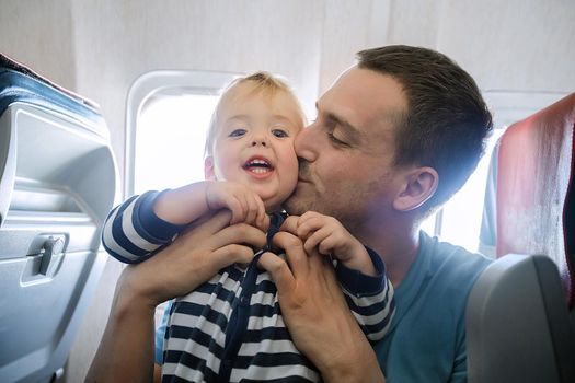 Father and baby son during flight on airplane going on vacations. Dad kisses his son on the plane. Air travel with baby, child and family concept.