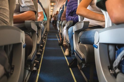 cabin of airplane with unrecognizable passengers on seats waiting to take off.