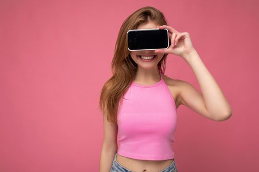 Photo of beautiful smiling young woman good looking wearing casual stylish outfit standing isolated on background with copy space holding smartphone showing phone in hand with empty screen display for mockup.