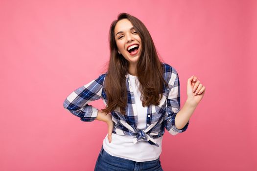 Photo portrait of young beautiful smiling hipster brunette woman in trendy blue and white shirt. Sexy carefree female person posing isolated near pink wall with empty space in studio. Positive model with natural makeup.