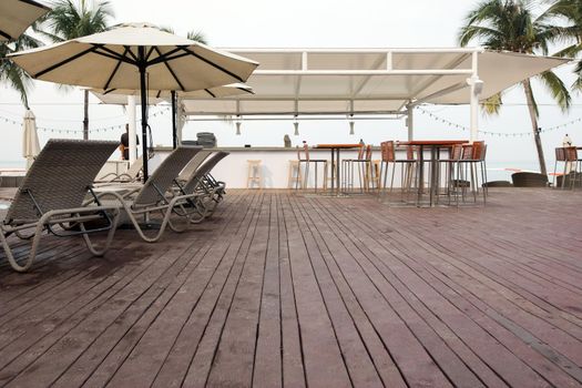 Wooden deck with lounge sunbeds and bar area on background of palms on tropical resort.
