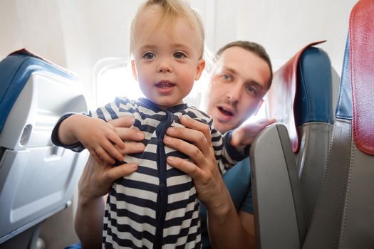 Father and baby son during flight on airplane going on vacations. Dad holding baby boy on a chair. Air travel with baby, child and family concept.