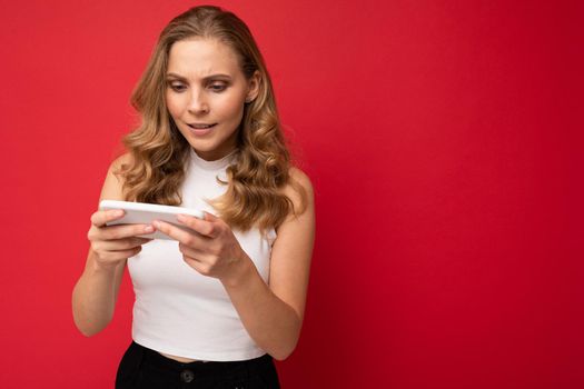Image of a shocked young beautiful woman posing isolated over red wall background play games by mobile phone