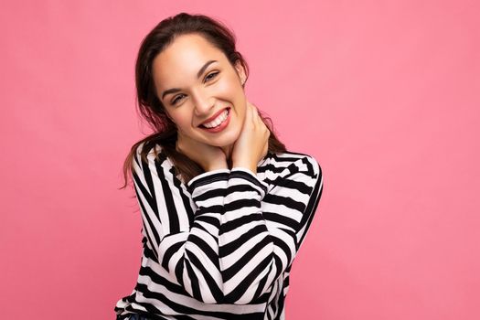 Photo portrait of young beautiful smiling hipster brunette woman in trendy pullover. Sexy carefree female person posing isolated near pink wall with empty space in studio. Positive model with natural makeup.