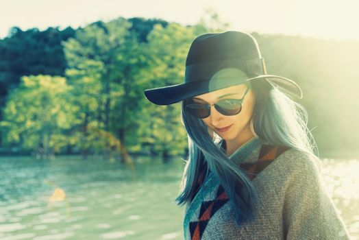 Beautiful young woman in hat and sunglasses resting on lake in summer at sunny day outdoor