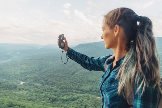 Traveler young woman searching direction with a compass in summer mountains.