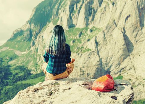 Traveler young woman sitting on rock stone in summer mountains, rear view. Image with instagram color