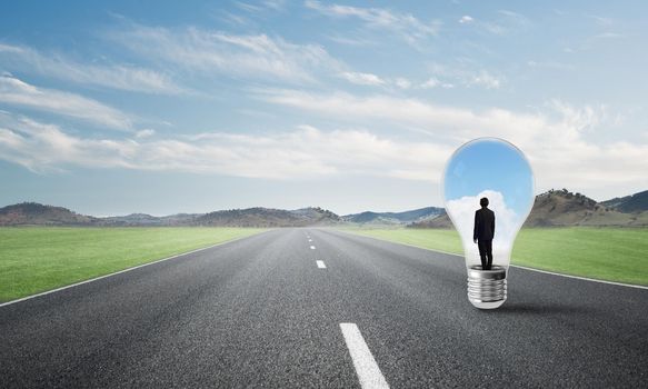 Young businessman trapped inside of light bulb on asphalt road