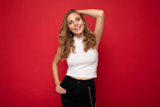 Photo portrait of young beautiful attractive positive smiling blonde woman wearing white top posing isolated over red background with copy space.