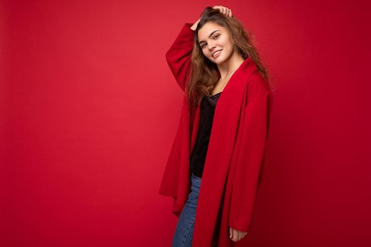 Young beautiful european stylish brunette woman wearing red cardigan isolated over red background with positive sincere emotions. Simple and natural looking at the camera. Free space.