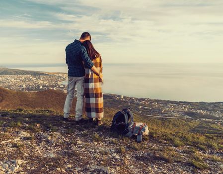 Travelers loving couple standing in the mountains and enjoying view of sea, rear view. Man embracing a woman