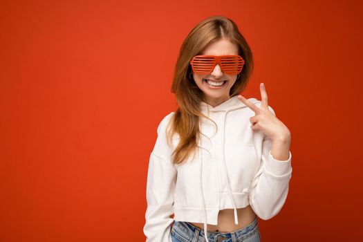 Photo shot of beautiful positive young blonde woman wearing casual clothes and stylish optical glasses isolated over colorful background wall looking at camera.