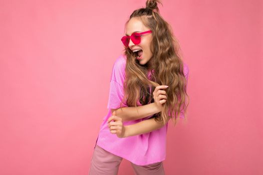 Attractive funny positive joyful young blonde woman wearing everyday stylish clothes and modern sunglasses isolated on colorful background wall looking to the side.