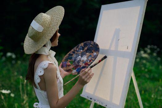 Woman in white dress paints a picture on nature easel. High quality photo