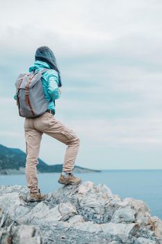 Unrecognizable explorer young woman with backpack standing on peak of cliff and enjoying view of sea in summer