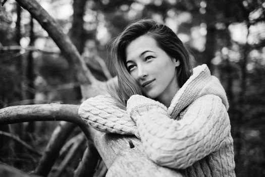 Beautiful young woman standing near a tree and looking dreamy into the distance. Monochrome image