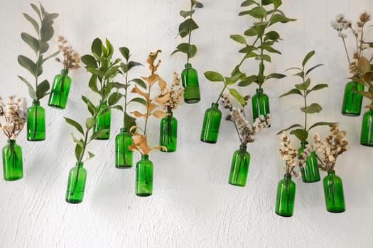 Wall with hanging green bottles and stick in flowers and green branches.