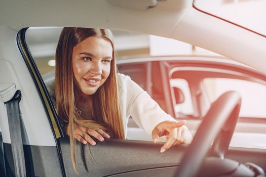 Young woman checking out a new car she is going to buy in car salon