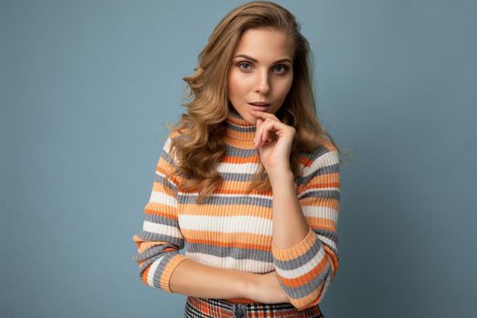 Young charming fascinating sexy positive happy blonde woman wearing casual striped pullover isolated over blue background with free space.