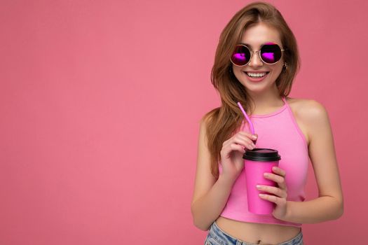 Photo of attractive young happy smiling blonde woman wearing everyday stylish clothes isolated over colourful background wall holding paper cup for cutout drinking tea looking at camera. copy space