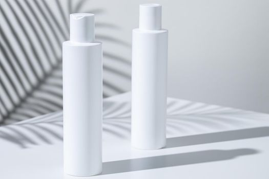 White plastic skincare tubes on a background of tropical plant shadow with copy space