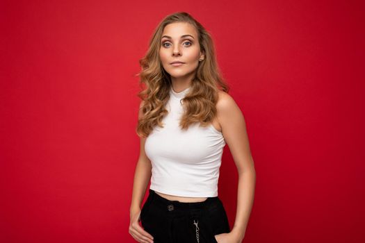 Portrait photo of young beautiful pretty self-confident assertive cool blonde woman with sincere emotions wearing stylish white top isolated over red background with free space.